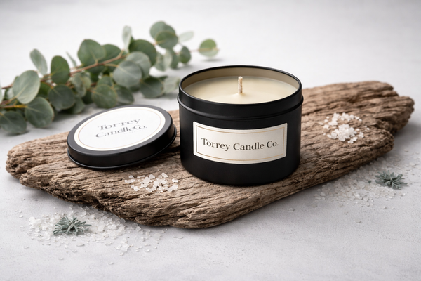 Torrey Candle Co. candle on a wooden log with eucalyptus leaves and small flowers.